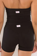 Rear view of a model wearing black high-waisted shapewear shorts with a wide ruched waistband and a small white brand tag reading E.LE.
