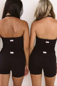 Two women shown from the back wearing matching black strapless biker shorts with a small white brand tag at the waistband, standing against a plain light background.
