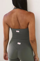 Rear view of a woman wearing a stone ribbed strapless tank top and matching high-waisted shorts with small white 'ELE' brand tags, against a plain off-white wall.